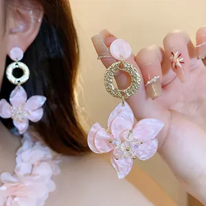 Close-up of pink resin flower pendant earrings with golden textured metal rings