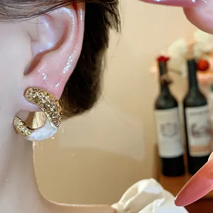 Close-up of model wearing textured gold C-shaped earrings with cream enamel drip details