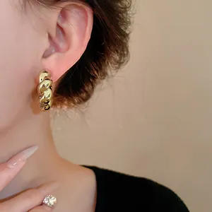 Primer plano de elegantes pendientes dorados retorcidos en forma de C en una modelo