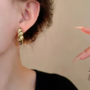 Primer plano detallado de elegantes pendientes de metal dorado retorcido en forma de C