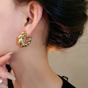Primer plano de pendientes de aro en C retorcidos de metal dorado en la oreja