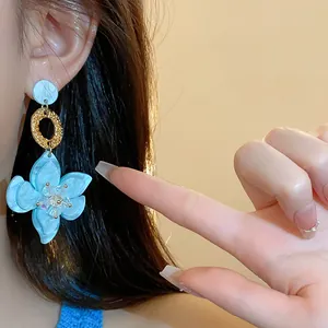 Close-up of light blue resin flower dangle earrings with gold accents worn by a model