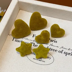 Detailed close-up of moss green flocked heart and star stud earrings on a fabric tray.