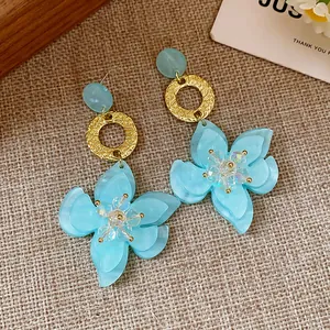 Close-up detail of blue resin flower earrings with textured gold hoops on a woven background