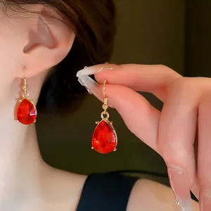 Elegant red teardrop rhinestone dangle earrings with gold finish shown on an Asian model
