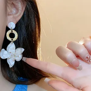 Close-up of elegant white resin flower drop earrings with golden textured metal rings