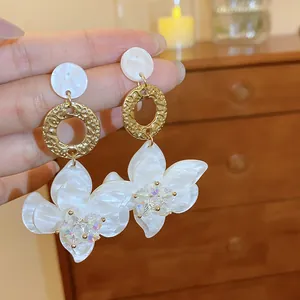 Detailed view of elegant white resin flower drop earrings with golden textured metal rings