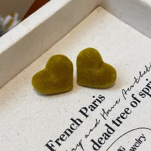 Detailed view of olive green flocked heart stud earrings on beige fabric background.