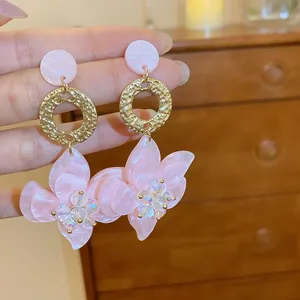 Detail of pink resin flower earrings with gold textured rings and silver needles.