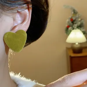 Close-up detail of a stylish green flocked heart-shaped stud earring on a model's ear