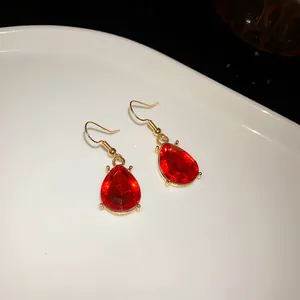 Macro detail shot of elegant red teardrop rhinestone earrings with gold hooks on white.