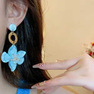 Elegant detail shot of light blue resin flower drop earrings with a textured golden ring