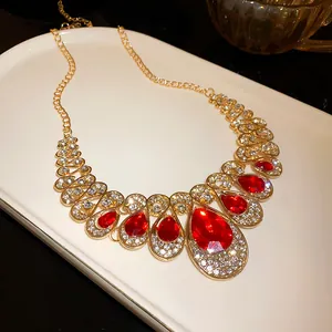 Macro detail of elegant gold necklace featuring red teardrop crystals and rhinestones