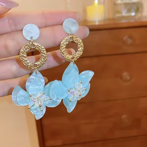 Detailed view of elegant light blue resin flower earrings with gold textured rings.