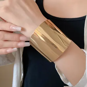 Nahaufnahme eines breiten glänzenden goldfarbenen Metall-Armreifs am Handgelenk getragen.