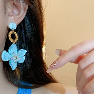 Detailed view of a light blue resin flower pendant earring worn by a model with long hair