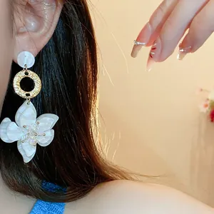 Close-up of white resin flower drop earrings with golden textured ring and crystals.