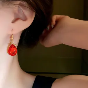 Close-up of elegant red teardrop earring on model showing delicate gold setting.
