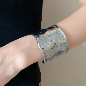 Detailaufnahme eines breiten gehämmerten silbernen Metallarmbands an einem Frauenhandgelenk.