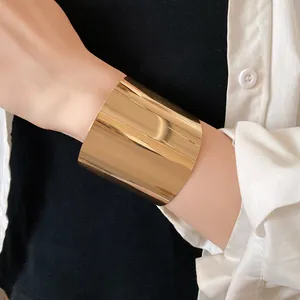Detailansicht eines minimalistischen breiten vergoldeten Armreifs an einem Handgelenk