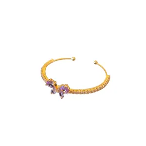 Bracelet jonc ouvert doré avec papillon en zircon violet et accents pavés sur fond blanc