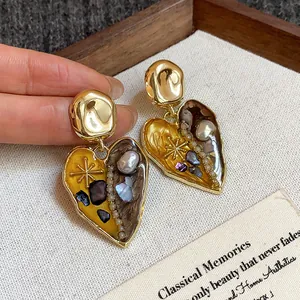 Dettaglio raffinato di orecchini a cuore in oro vintage con intarsi in perla e conchiglia