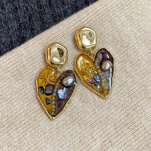 Dettaglio di eleganti orecchini vintage a cuore con intarsi di perle e conchiglie.