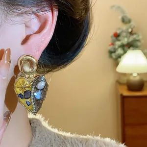 Dettaglio macro di un orecchino a lobo vintage a cuore con perle e pietre su modella