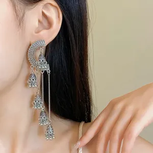 Close-up detail of vintage bohemian long tassel earrings with silver bell charms on model.