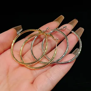 Large minimalist geometric metal hoop earrings in gold and silver finishes held by hand