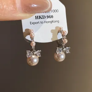 Detailed close-up of champagne pearl drop earrings with crystal bow accents on a tag