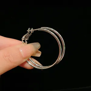 Detailed close-up of minimalist silver-tone round metal hoop earrings held by a hand.