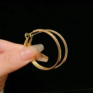 Detail shot of classic golden hoop earrings held by a hand on a black background