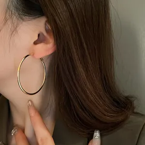 Macro detail showing a minimalist gold-tone round hoop earring worn by a model