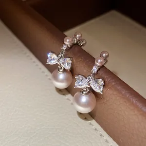 Macro detail of bow-knot pearl earrings featuring pink pearls and cubic zirconia