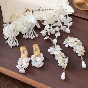 A detailed close-up showing various elegant white floral pearl earrings on a wooden background