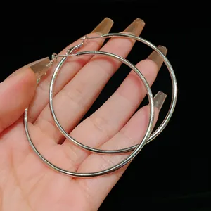 Macro view of large minimalist silver hoop earrings held in hand to show size and shine.