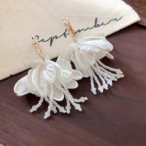 Close-up detail of elegant white petal flower earrings with bead tassels and gold hooks