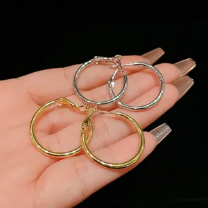 Detailed close-up view of gold and silver round hoop earrings held in hand for scale