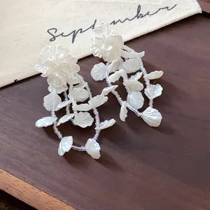 Macro detail of elegant white floral tassel earrings with iridescent beaded chains.