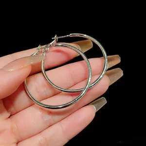 Macro view of minimalist silver hoop earrings held by hand on black background