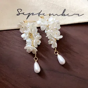 Elegant white floral drop earrings with teardrop pearls on a rustic wood background