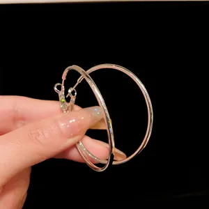 Close-up view of minimalist large silver hoop earrings held by hand against a black background
