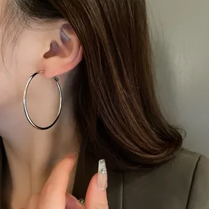 Close-up view of a minimalist silver metal hoop earring worn by a model in detail