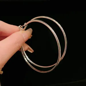 Detailed close-up view of minimalist large silver metal round hoop earrings held by hand