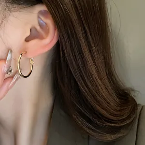 Close-up detail of minimalist gold hoop earrings on ear with elegant brown hair styling