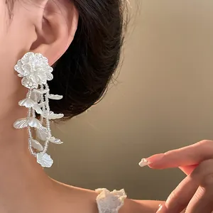 Close-up of elegant white flower dangle earrings with 18K gold plating on a model.