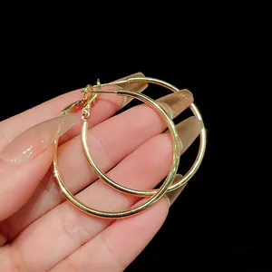 Close-up detail of large minimalist gold-tone metal hoop earrings held against black background