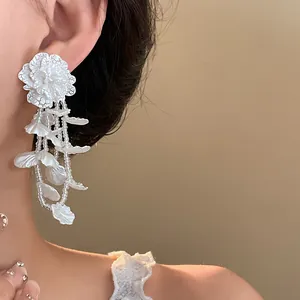 Close-up of elegant white floral lace earrings with beaded tassels and petals on a model