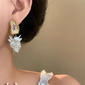 Close-up of 18K gold-plated earrings with square gems and white floral dangles